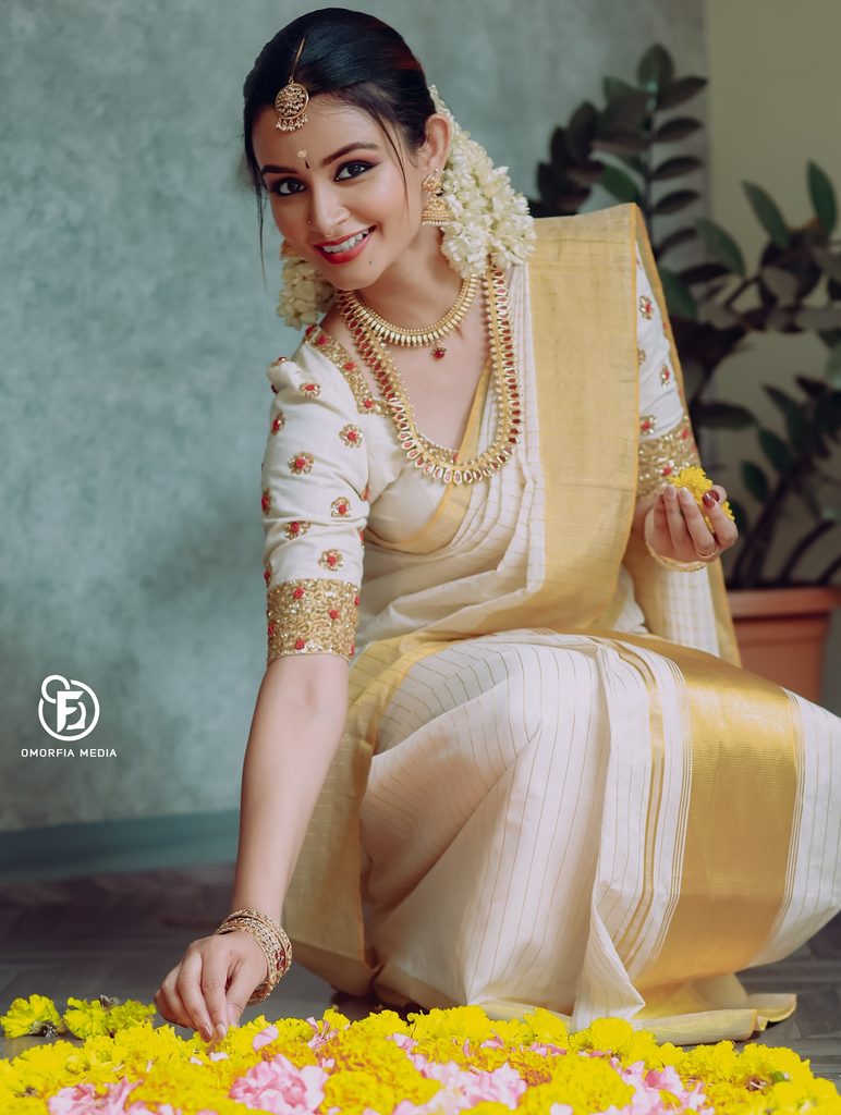 Actress sitting near Onam Pookkalam in Kasavu Saree pose